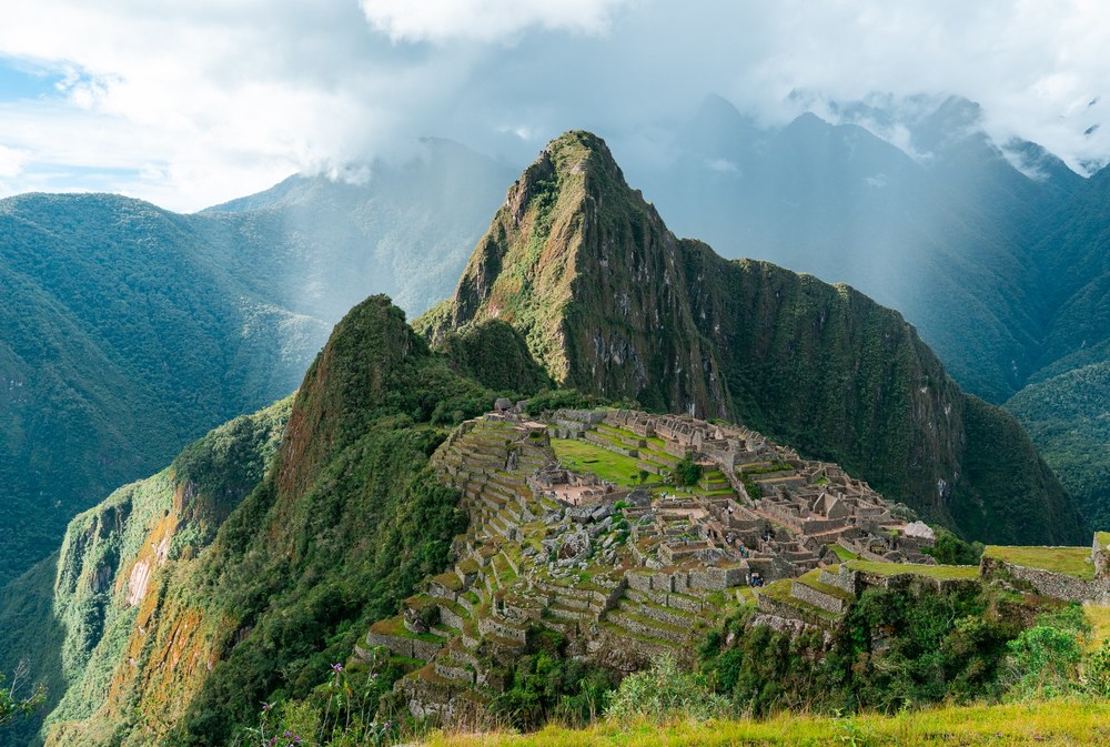 Stone terraces and ruins at Machu Picchu, Peru, sit beneath a dramatic mountain peak wrapped in clouds.
