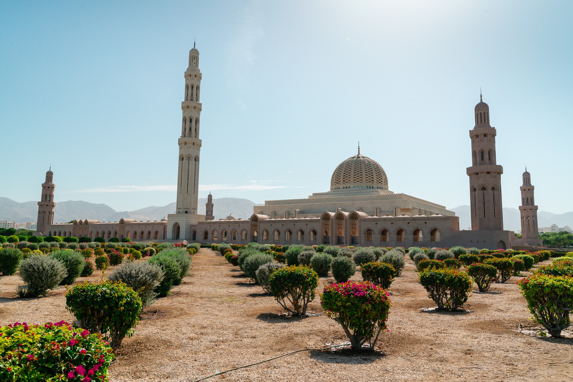The dome and minarets of Sultan Qaboos Grand Mosque rise beyond gardens and flowering shrubs in Muscat, Oman.