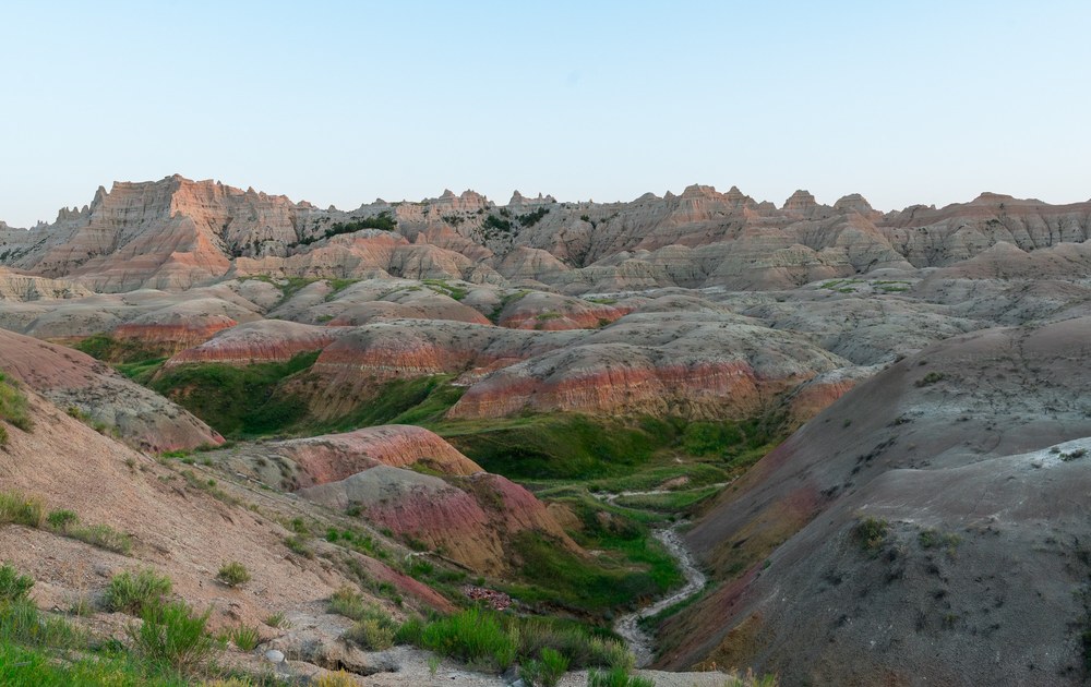 Bands of pink, red, and gray trace the ridges above a green valley in Badlands National Park.