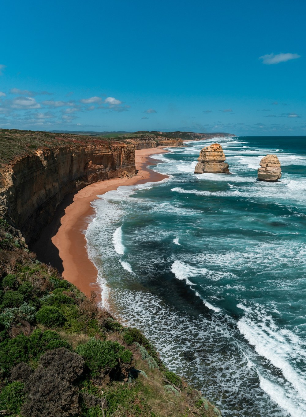 Waves roll toward the rugged coastline and limestone sea stacks of the Twelve Apostles, Australia.