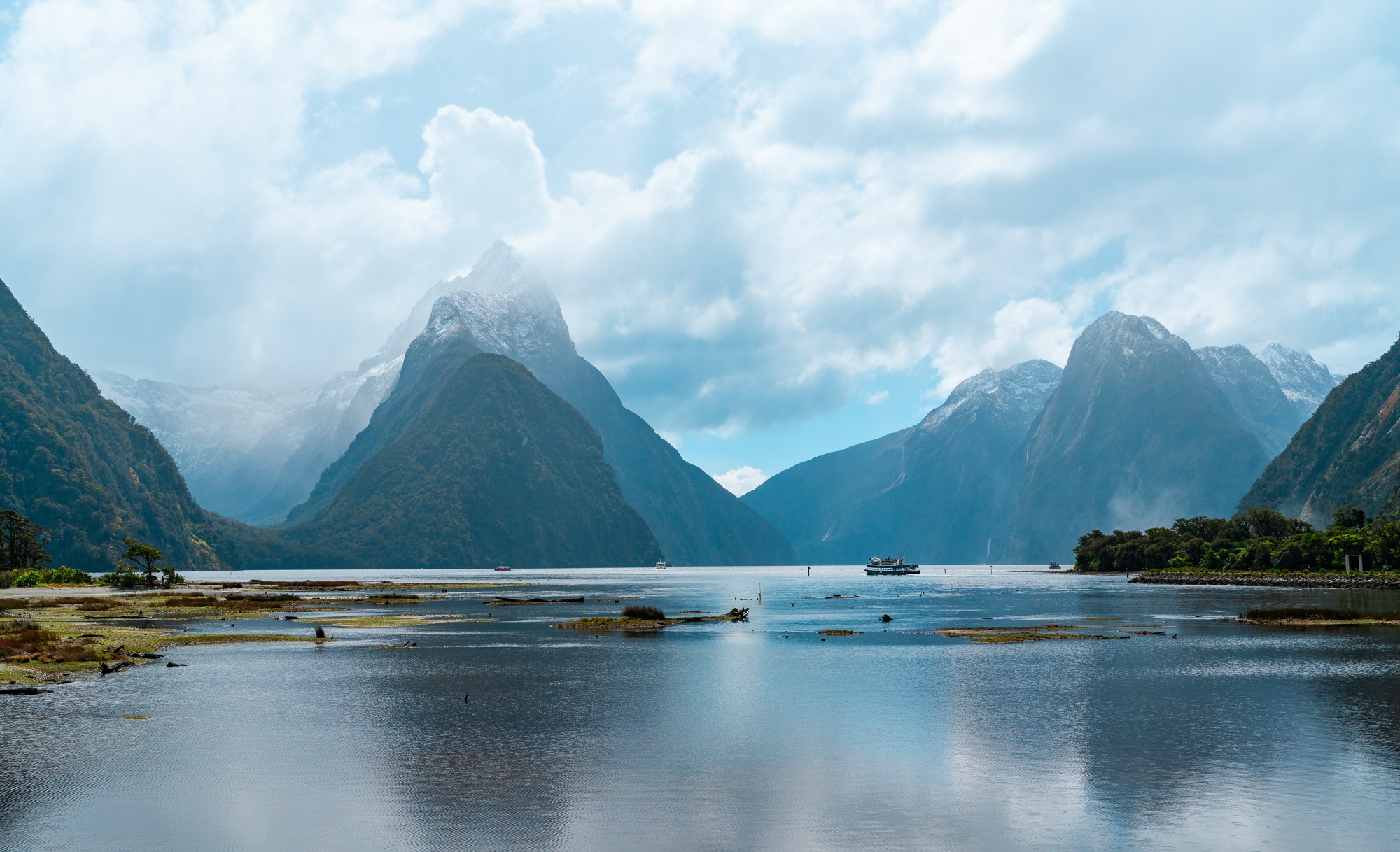 Cloud-wrapped mountains rise above the calm waters of Milford Sound, New Zealand.